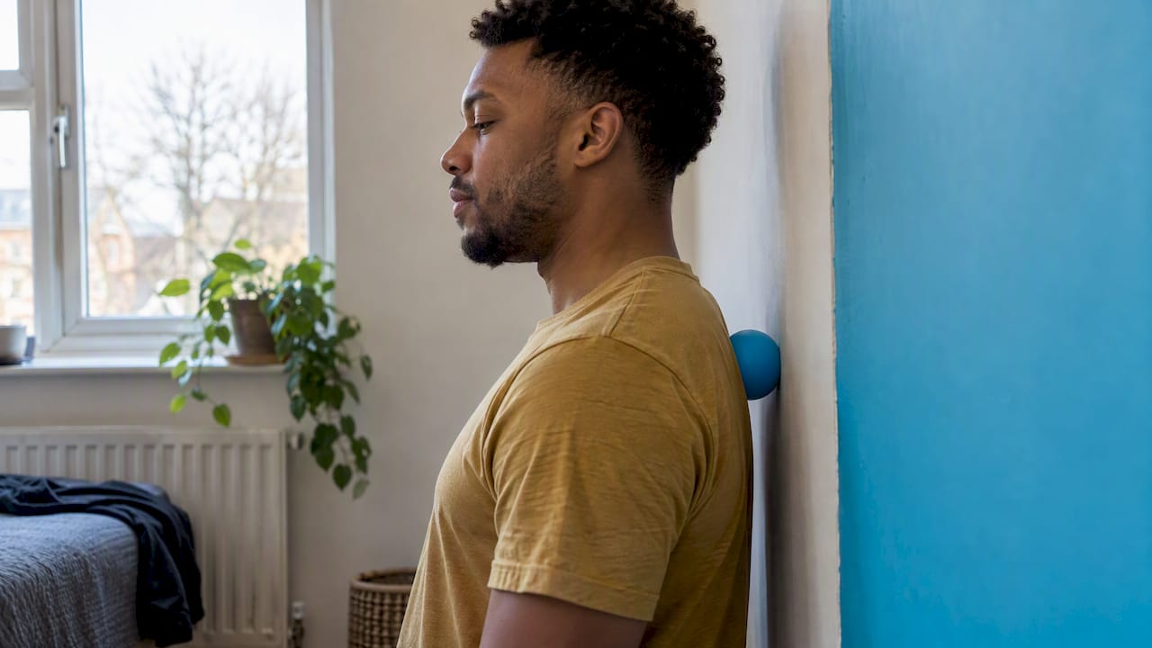 Man gently using a massage ball on his upper back